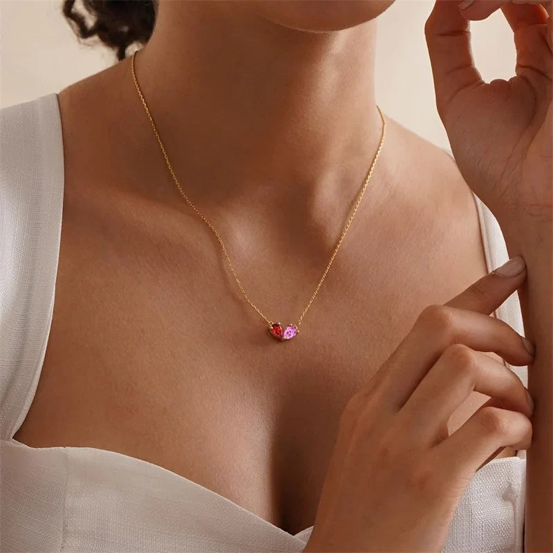 Two pear-shaped stones set together as one heart on a gold-color chain, worn at the collarbone
